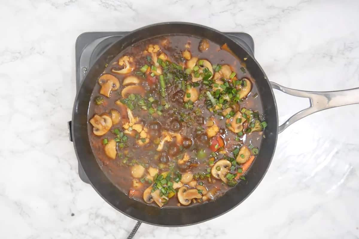 Les légumes prêts dans une sauce chaude à l'ail garnis d'oignons de printemps.