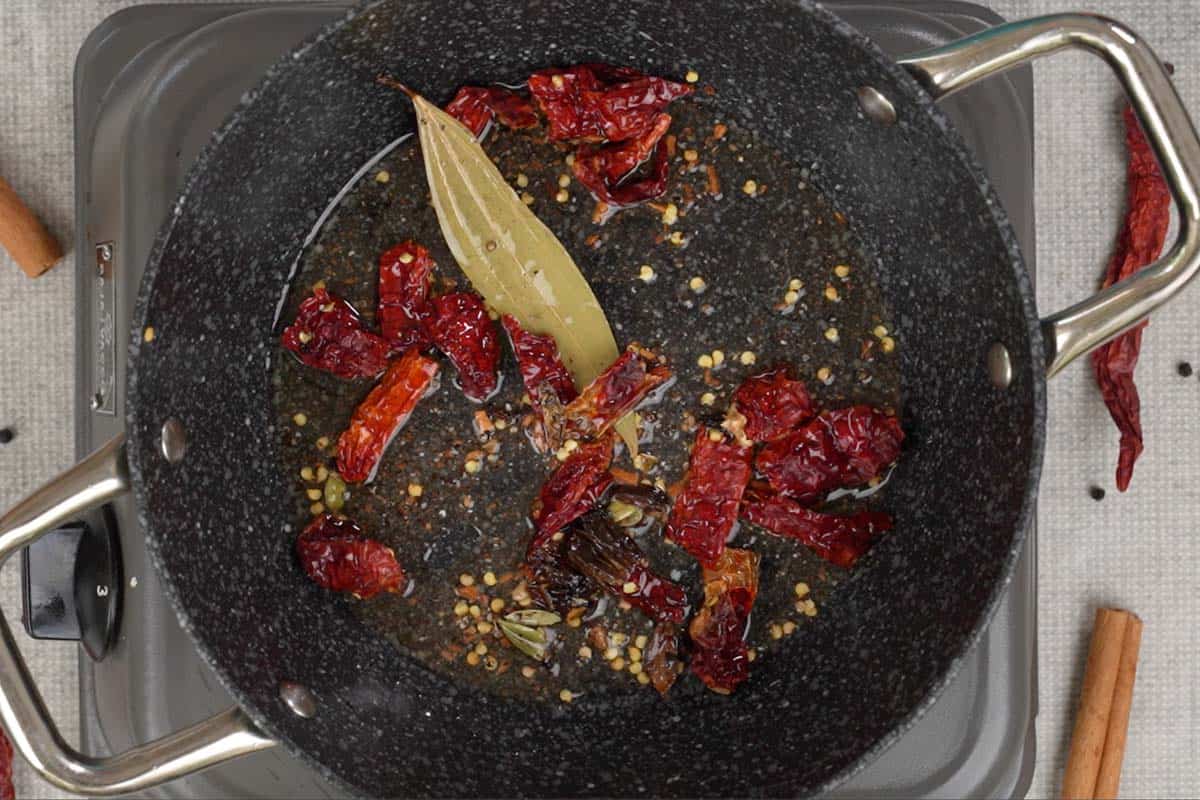 Crushed spices, bay leaf and dry red chilies added to hot oil in a pan.