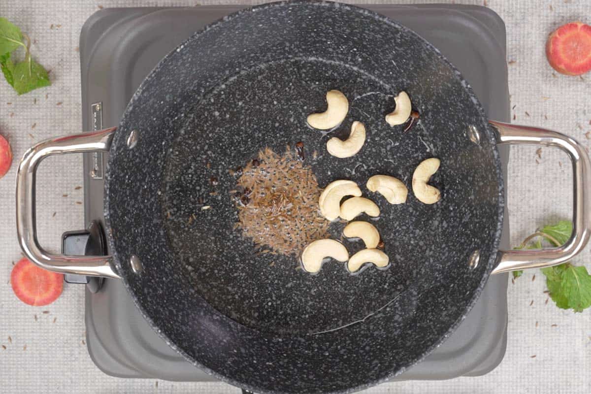 Cumin seeds, peppercorns, cloves and cashew nuts added to hot oil in a pan.
