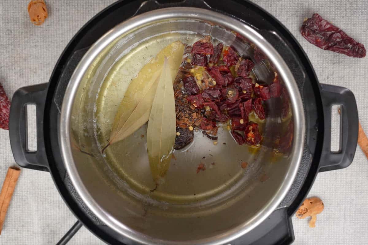 Crushed spices and dry red chilies added to hot oil in an instant pot.