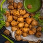A plate of crispy Kuttu Ke Pakore served with green chutney and a bowl of white yogurt, garnished with fresh coriander and green chilies, on a dark background.