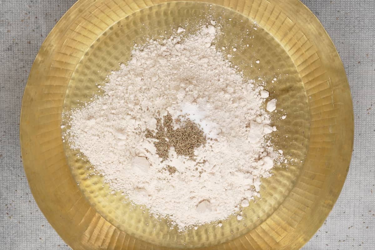 Whole wheat flour, oil, carom seeds and salt added to a large flat bowl.