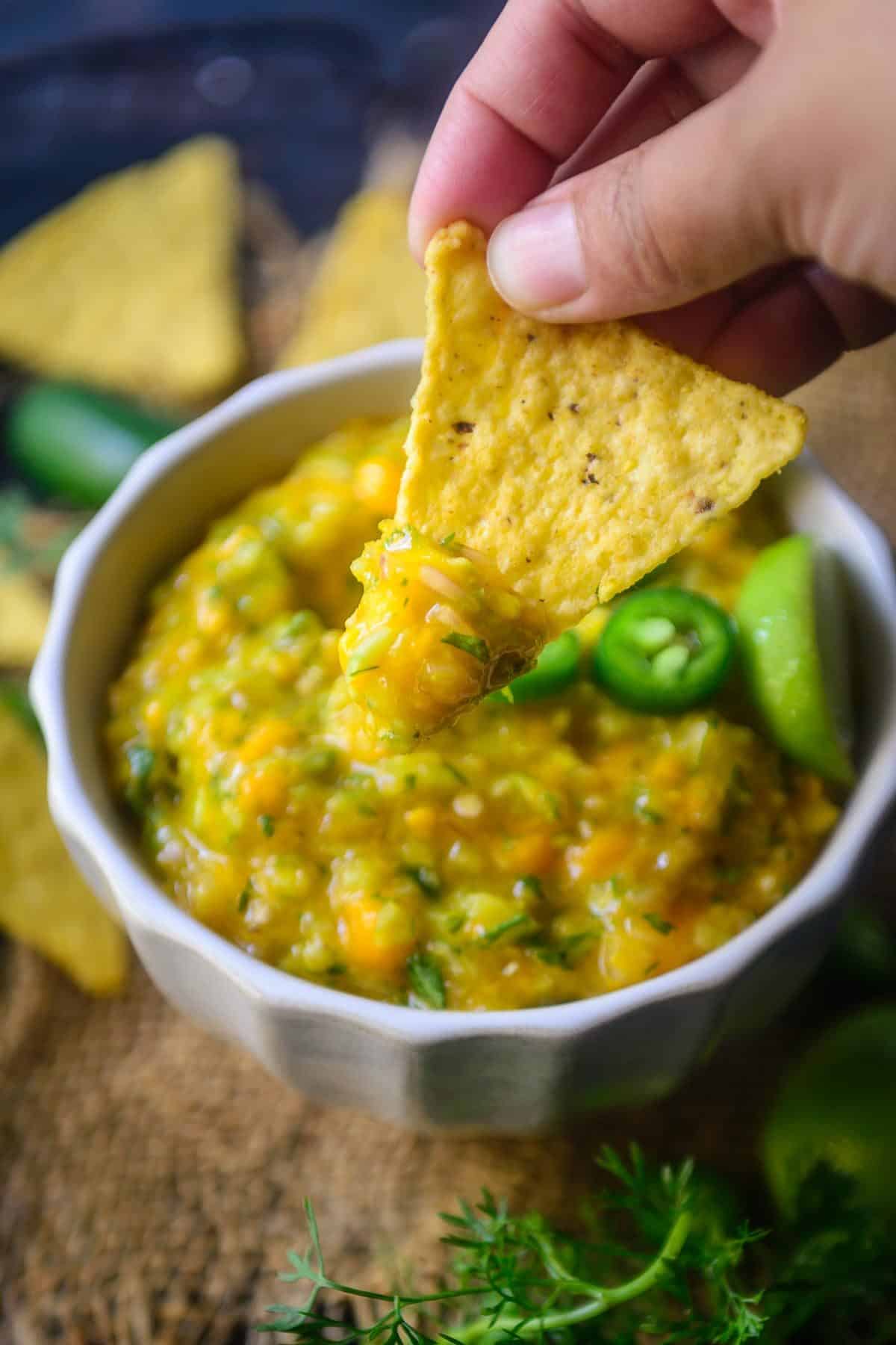 Scooping mango and cucumber salsa with a nacho chips.