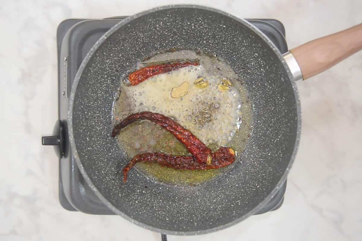 Cardamom, cloves, peppercorns, cinnamon, dry red chillies, cumin seeds and hing added in the pan.