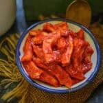 A white bowl with a blue rim filled with Hing ka Achar, placed on a piece of burlap fabric with a spoon in the background.