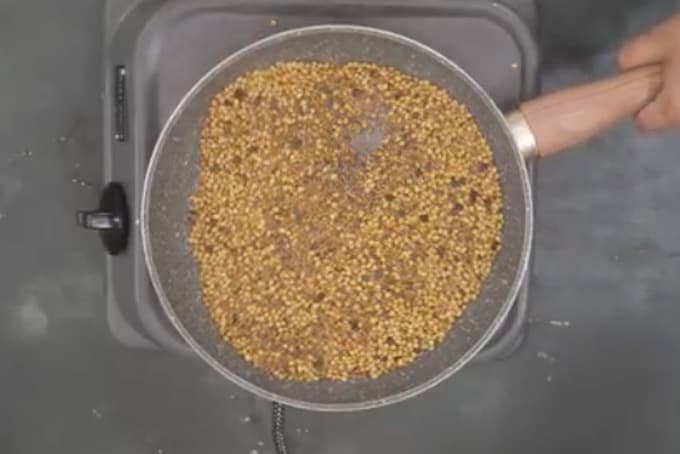 Coriander seeds, cumin seeds, mustard seeds, fenugreek seeds and black peppercorn roasting in a pan.