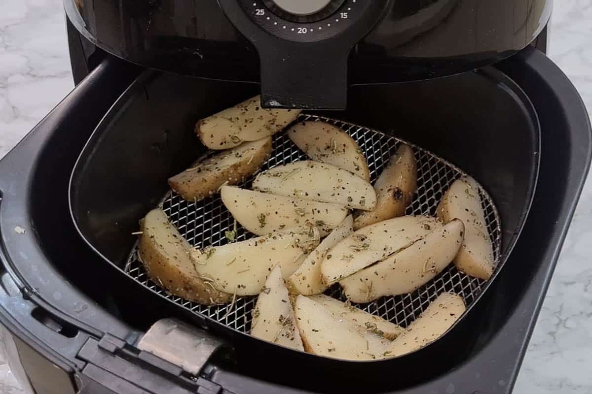 Potato wedges lined in the basket of the air fryer.
