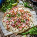 A crisp Masala Papad topped with chopped onions, tomatoes, fresh cilantro, and green chili, served on parchment paper with lemon wedges and extra herbs on a rustic metal tray.