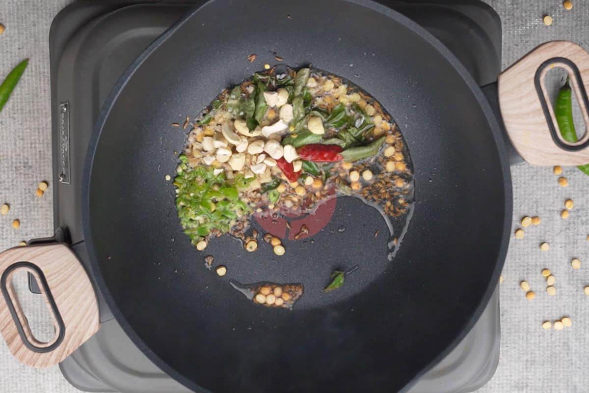 Asafetida, curry leaves, green chilies, dry red chilies, ginger and cashew nuts added to the pan.