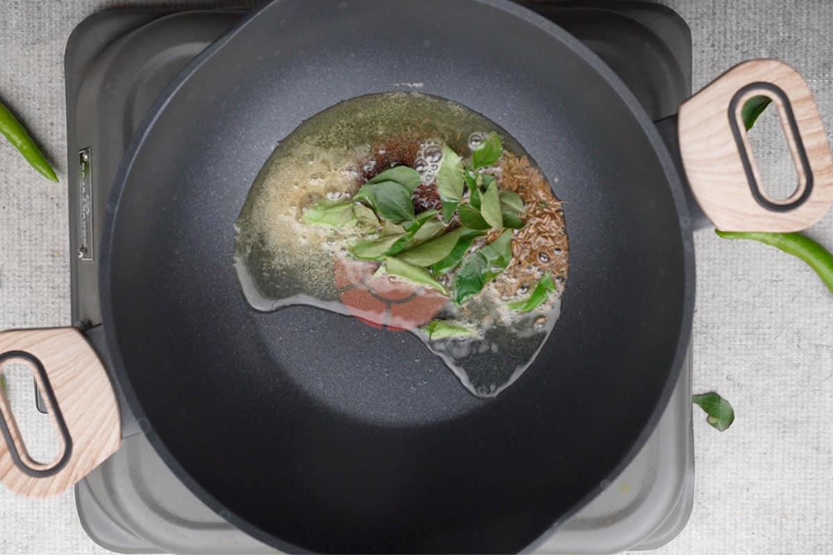 Mustard seeds, cumin seeds, dried red chilies, hing and curry leaves added to hot oil in a pan.