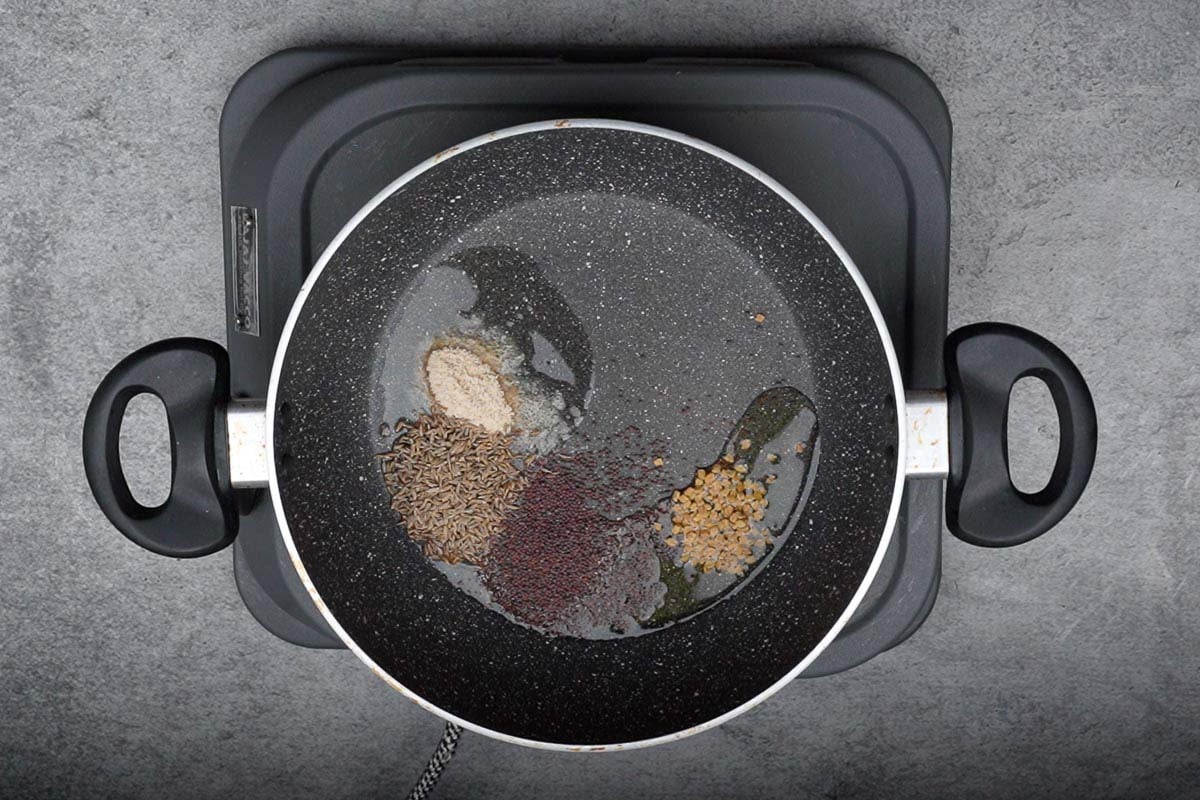 Asafetida, cumin seeds, mustard seeds and fenugreek seeds added to hot oil in a pan.