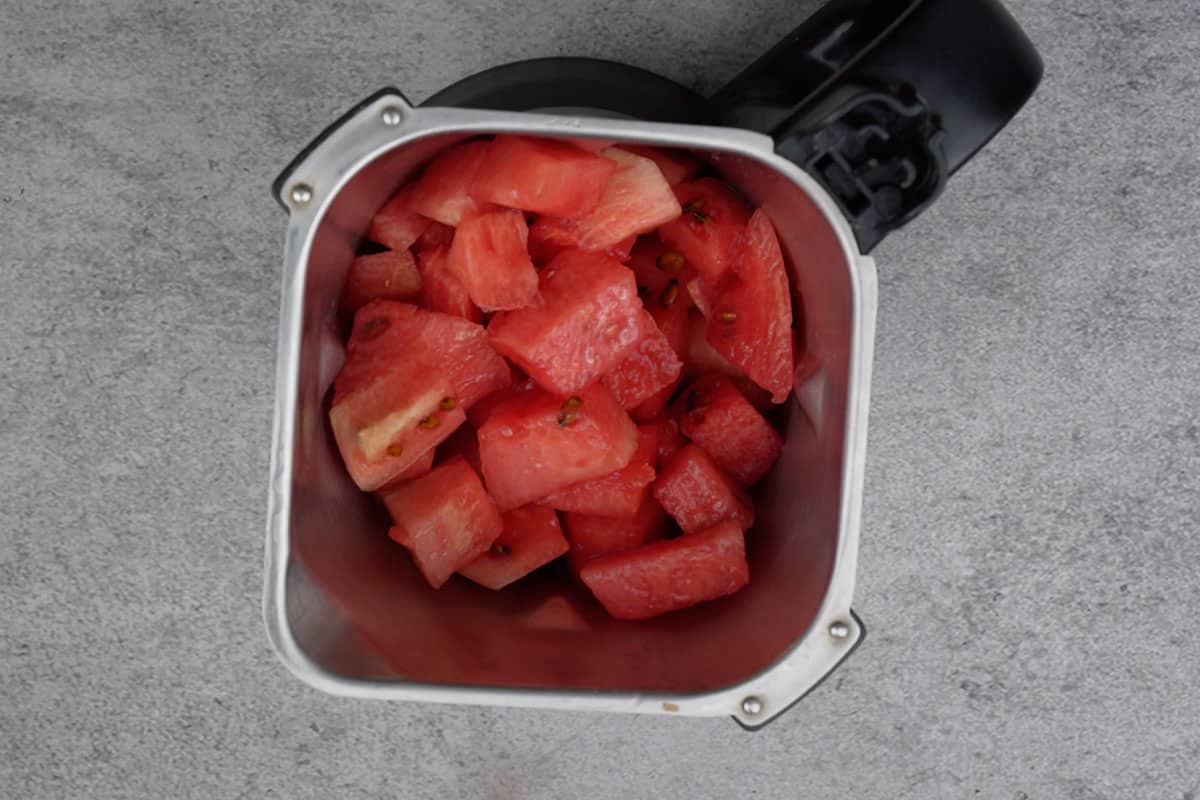 Watermelon cubes added to a blender.