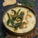 A bowl of South Indian rava pongal garnished with curry leaves, roasted cashews, and spices, with pieces of crispy papad kept on the side.