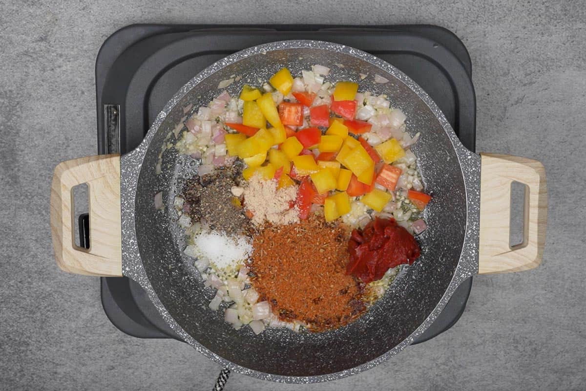 Bell peppers, tomato paste, salt, pepper, cajun seasoning and chicken broth powder added to the pan.