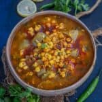 A bowl of spicy Indian Lauki Chana Dal garnished with fresh cilantro. Slices of lemon, green chili, and cilantro are placed around the bowl on a dark blue textured surface.