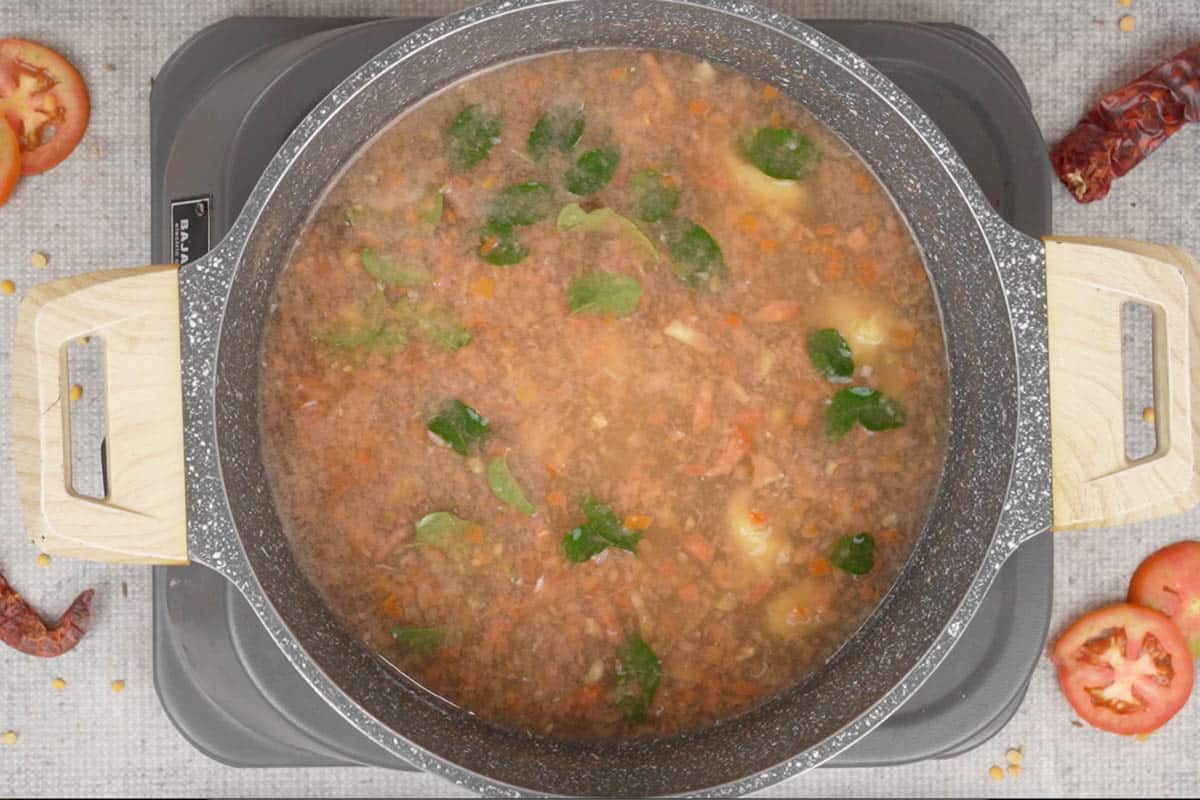 Tomato paste, tuvar dal, tamarind paste, garlic, curry leaves and water added to a pan.