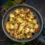 A bowl of Vrat Wale Sookhe Aloo, garnished with chopped herbs and sits on a dark surface, with fresh green chilies and coriander in the background.
