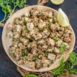 A plate of farali arbi fry garnished with fresh coriander, lemon wedges, and a green chili on a dark textured surface.