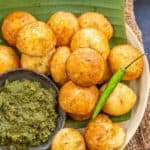 A plate of golden-brown Vrat Ke Appe served on a banana leaf with green chutney, garnished with a green chili, accompanied by fresh herbs and a glass of chai.