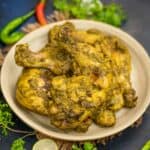 A beige plate with pieces of Chicken Cafreal garnished with fresh coriander, green chilies, and lime slices, set on a dark surface.