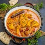 A bowl of vibrant Boneless Chicken Curry garnished with herbs and a cinnamon stick, surrounded by pieces of naan bread and fresh coriander on a dark textured surface.