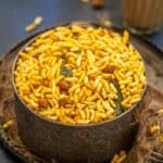 A bowl filled with spicy Murmura Namkeen (puffed rice snack), garnished with curry leaves and peanuts, is placed on a decorative tray with a glass of masala chai in the background.