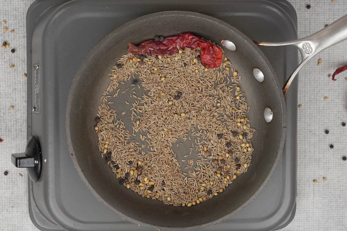 Cumin seeds, black peppercorns and dry red chili roasting in a pan.