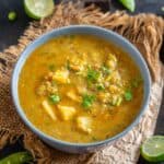A blue bowl filled with Matar ka Nimona, garnished with fresh cilantro, rests on a rustic jute mat, with a halved lime and green chili in the background.