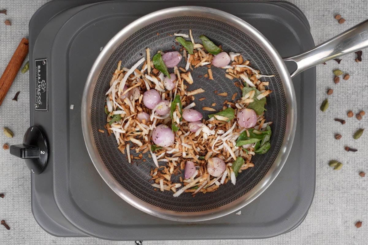 Dark roasted coconut with peeled shallots and curry leaves added to the skillet.