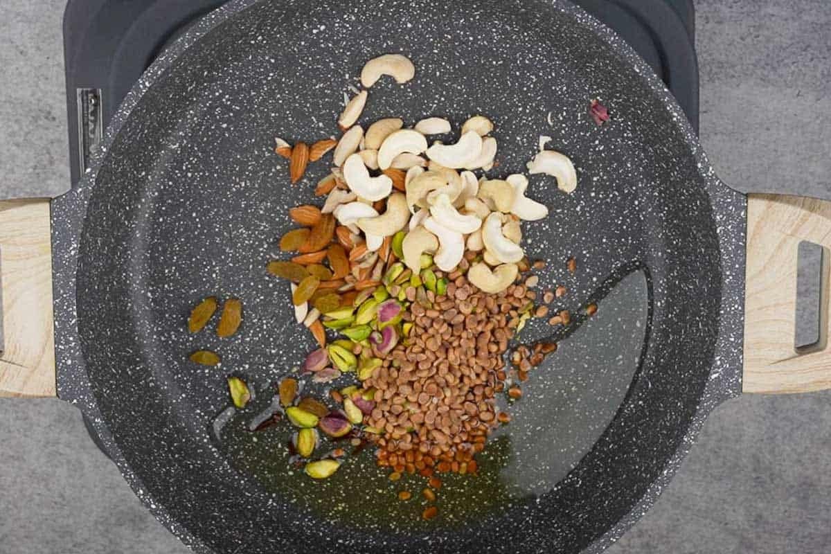 Dried nuts and fruits added to hot ghee in a pan.