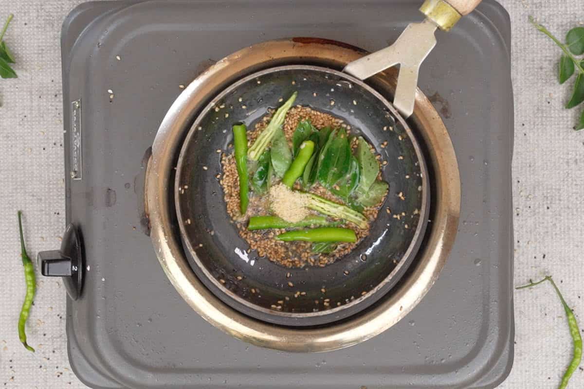 Mustard seeds, sesame seeds, green chilies, curry leaves and hing added to hot oil in a pan.