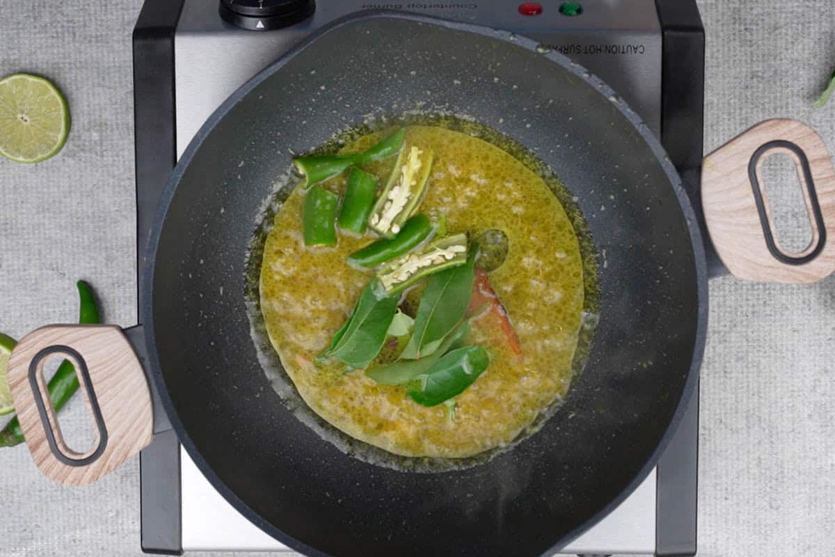 Whole spices, curry leaves and green chilies added to the pan.