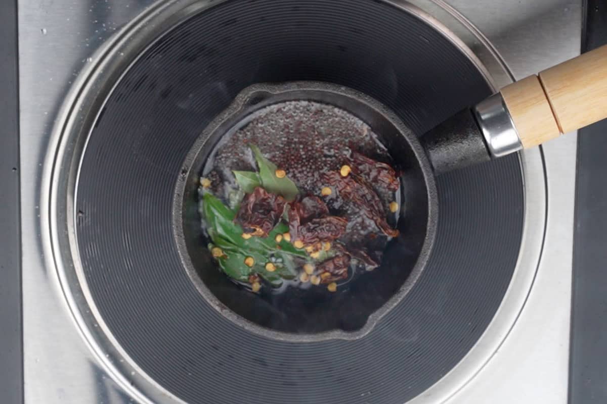 Dried red chilies, curry leaves and mustard seeds added to hot oil in a small pan.