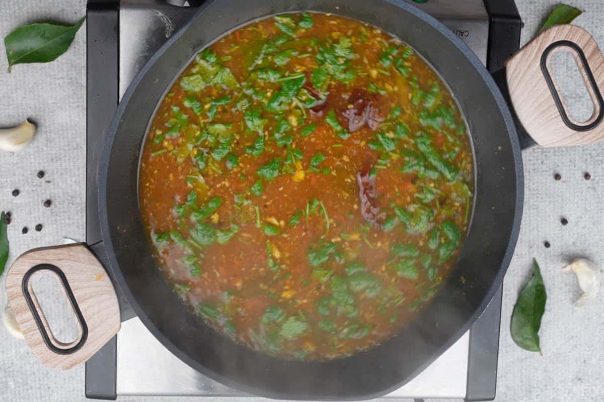 Ready pepper rasam garnished with chopped cilantro.
