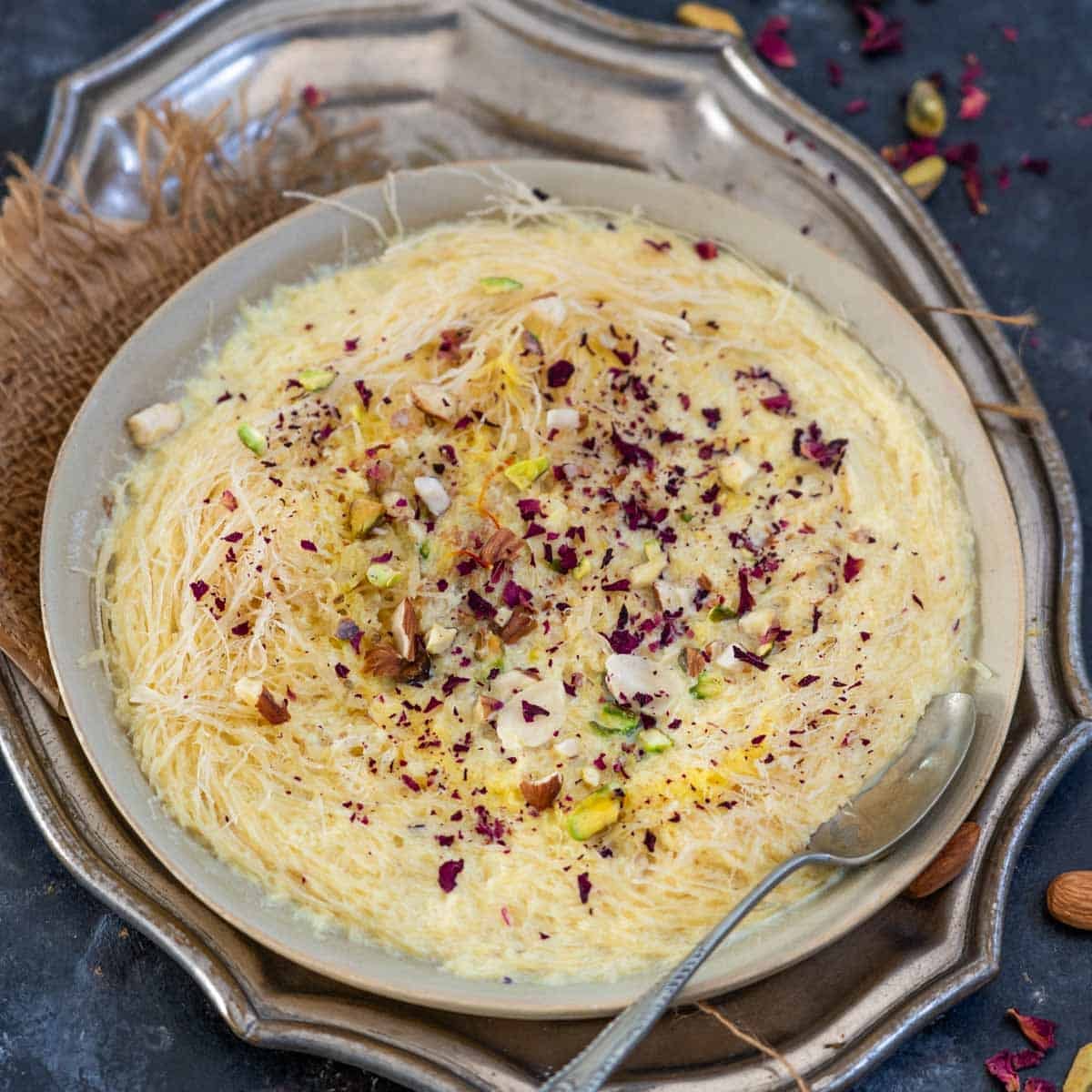 Saffron-flavored doodh pheni garnished with chopped nuts and rose petals, served hot on a plate.