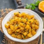 A white bowl filled with fresh Orange Chaat garnished with herbs, placed on a piece of burlap with a gold fork nearby and orange slices and mint leaves in the background.