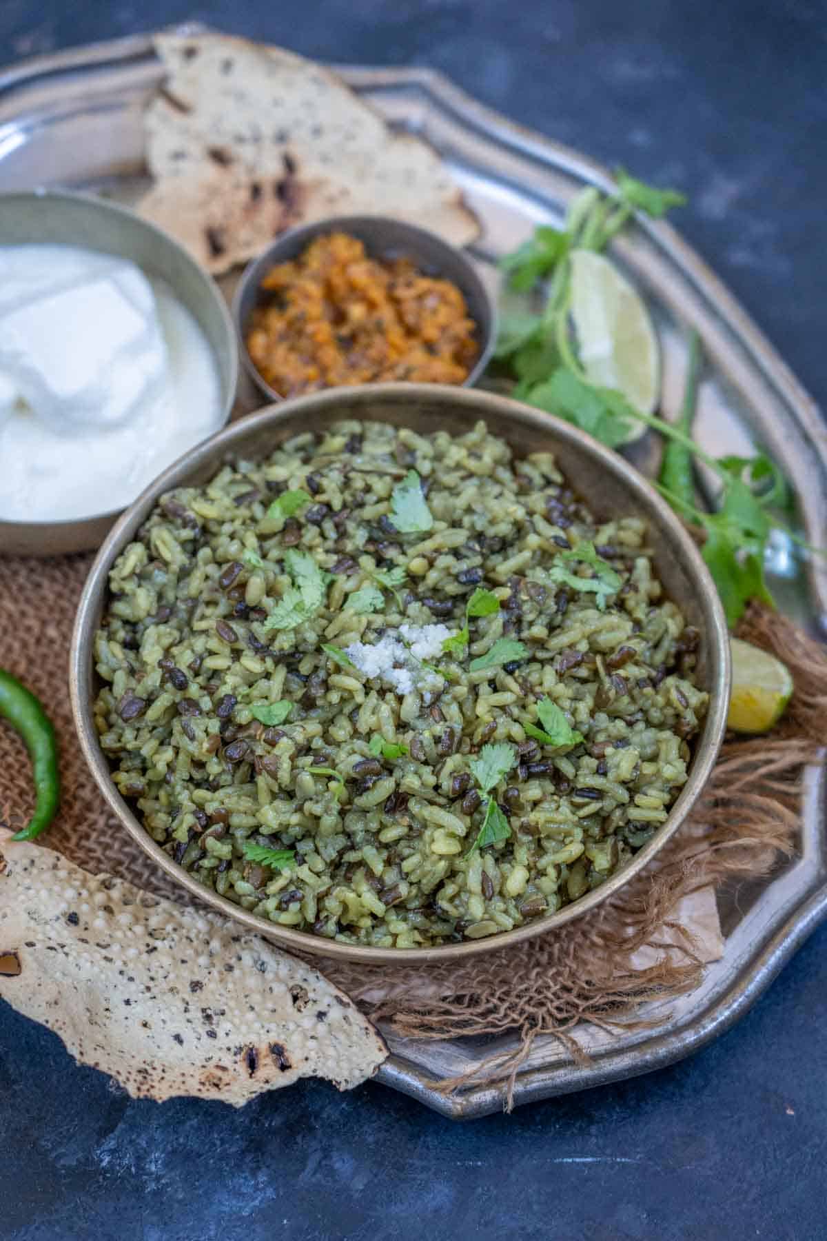 Urad dal khichdi served in a bowl and served with yogurt, pickle and papad.