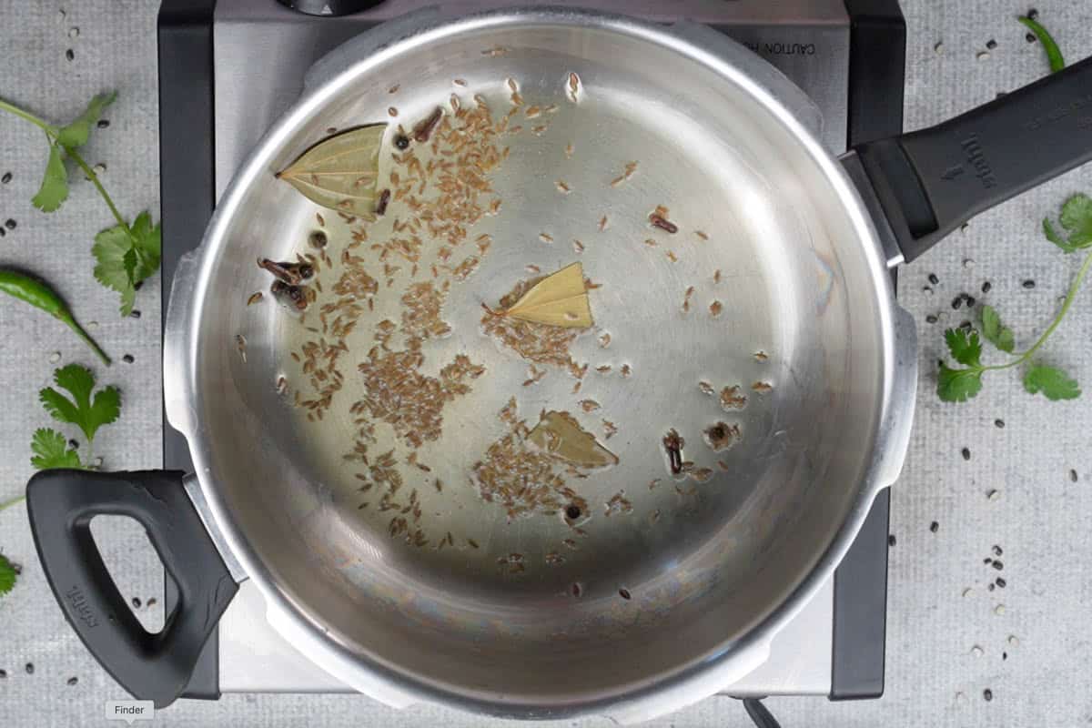 Cloves, bay leaf, peppercorns and cumin seeds added to hot oil in a pressure cooker.