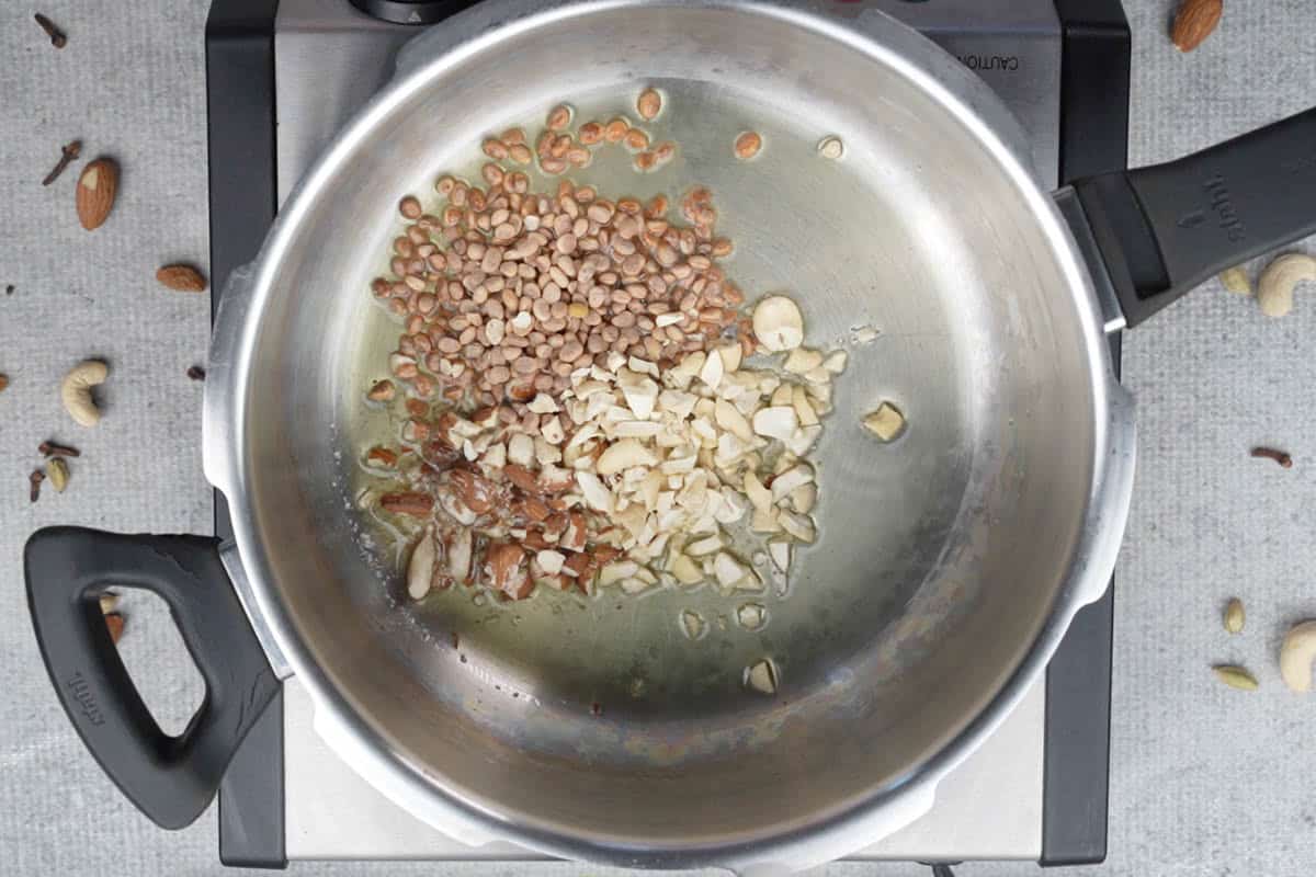 Almonds, cashews and chironji added to hot ghee in a pressure cooker.