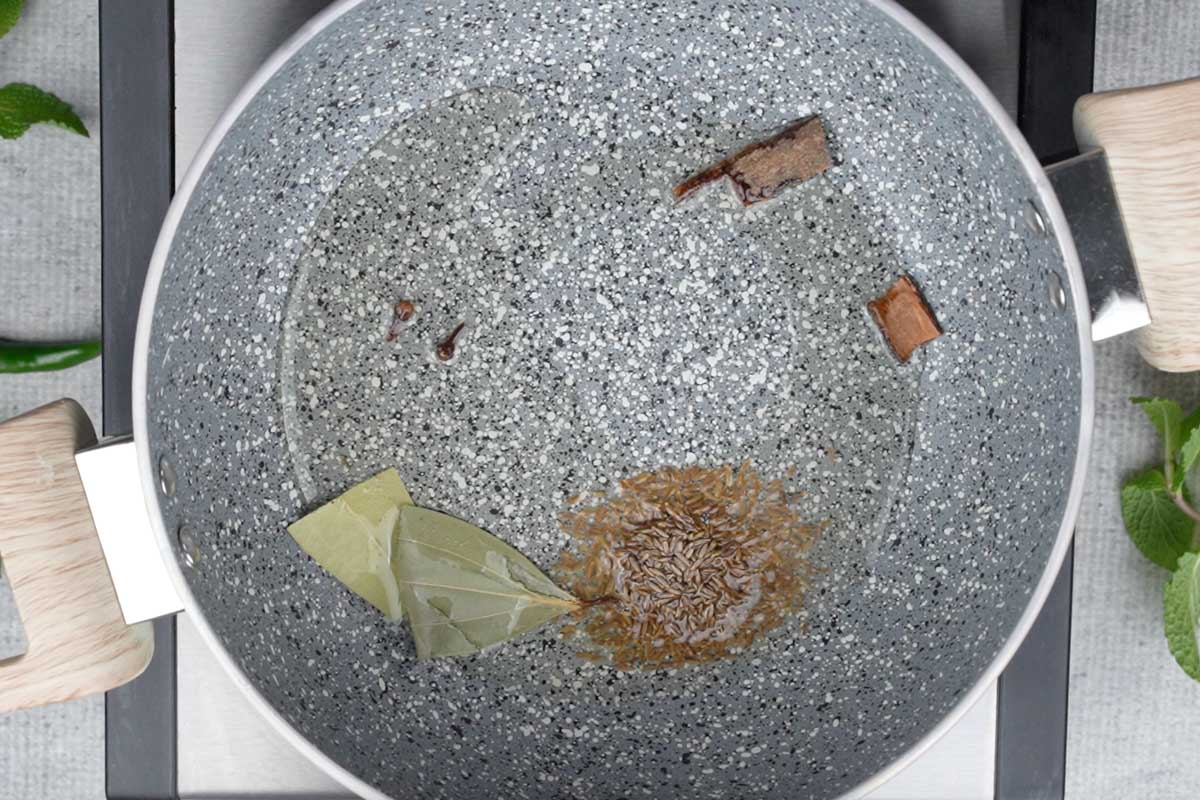 Whole spices added to hot oil in a pan.