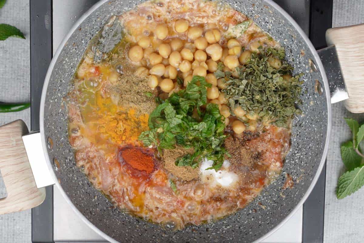 Cooked chickpeas, spice powders, salt, mint leaves and lime juice added to the pan.