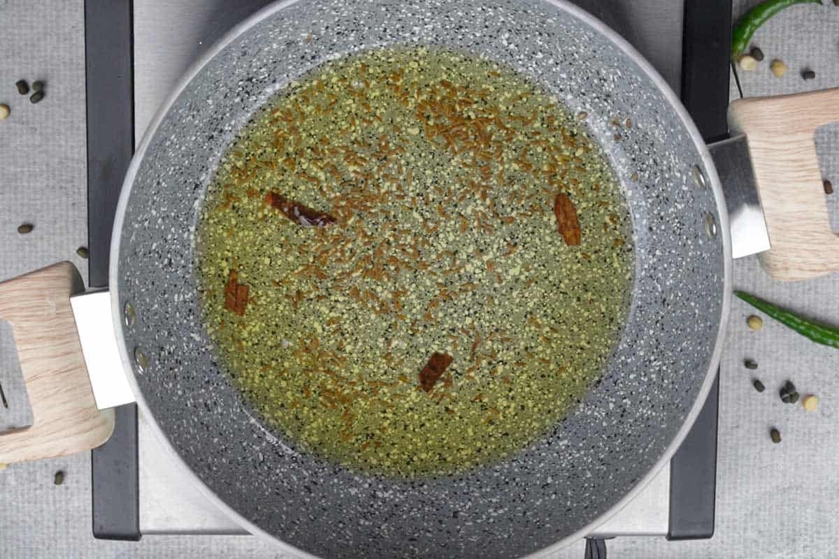 Cinnamon and cumin seeds added to hot ghee in a pan.