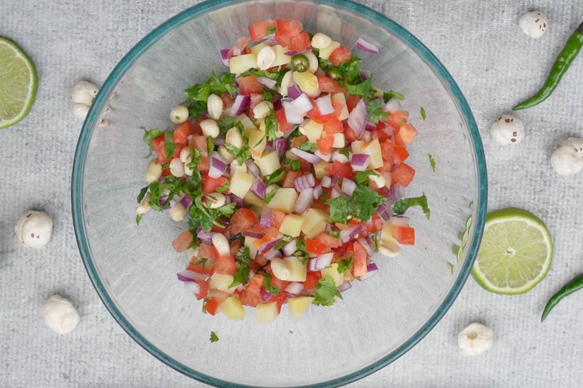 Onions, tomatoes, green chili, cilantro, boiled potatoes and roasted peanuts mixed in a bowl.