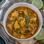 A bowl of Methi Chicken curry served on a rustic silver plate, garnished with slices of lime and sprigs of fresh methi in the background.