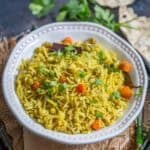A white bowl filled with Chaas Wala Pulao, featuring yellow rice mixed with peas, carrots, and garnished with fresh cilantro. The bowl sits on a rustic woven mat.