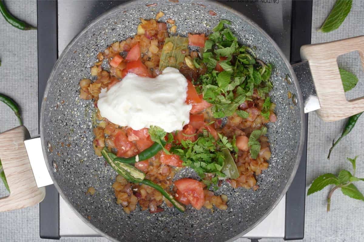 Tomatoes, yogurt, green chilies, cilantro and mint leaves added to the pan.