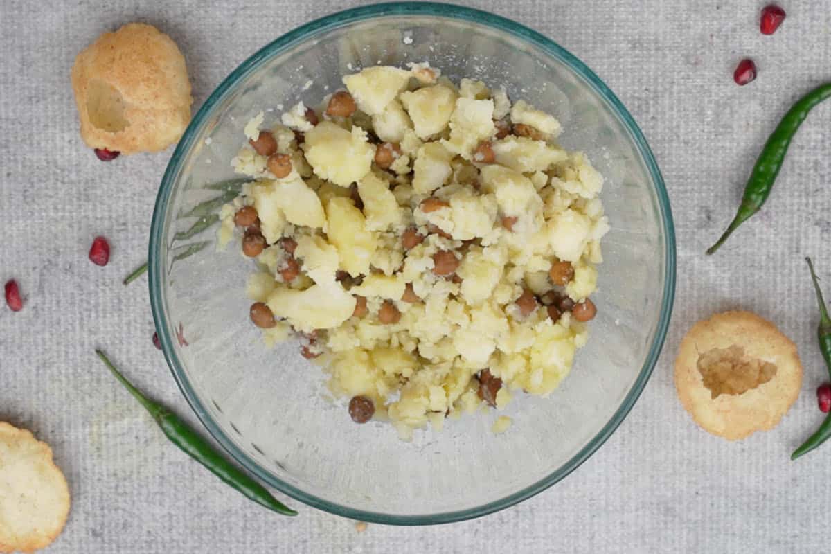 Boiled potatoes and cooked black chickpeas mashed in a bowl.