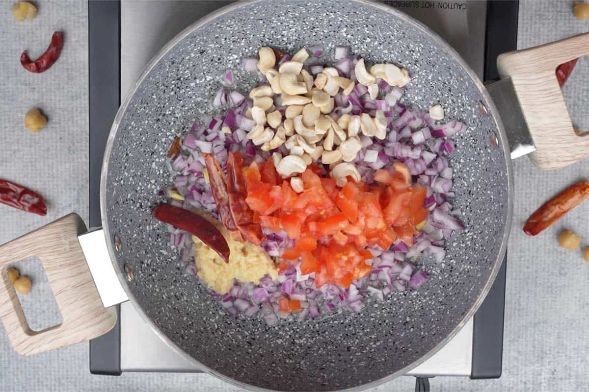 Onions, tomatoes, ginger-garlic paste, dried red chilies and cashews added to the pan.