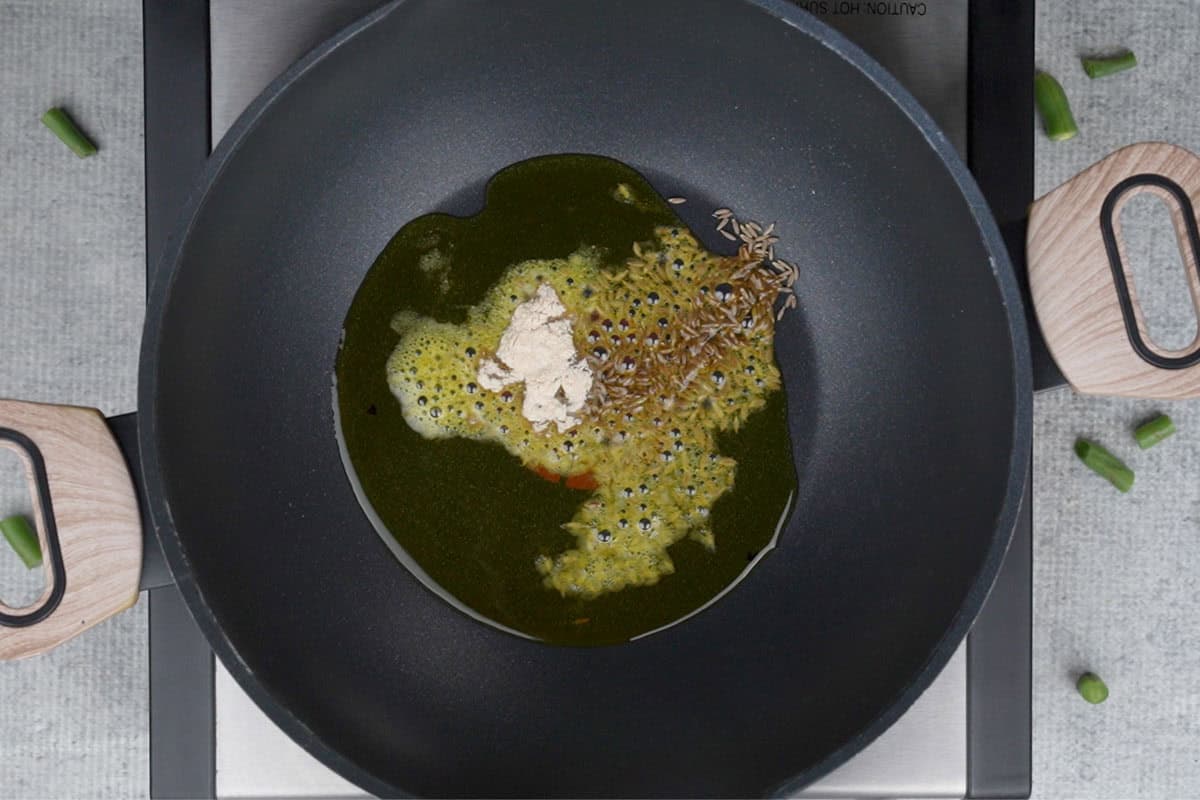Cumin seeds and hing added to hot oil in a pan.