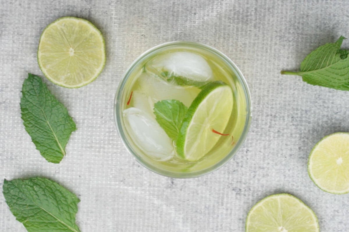 Saffron nimbu pani poured over ice and lime slices in a glass.